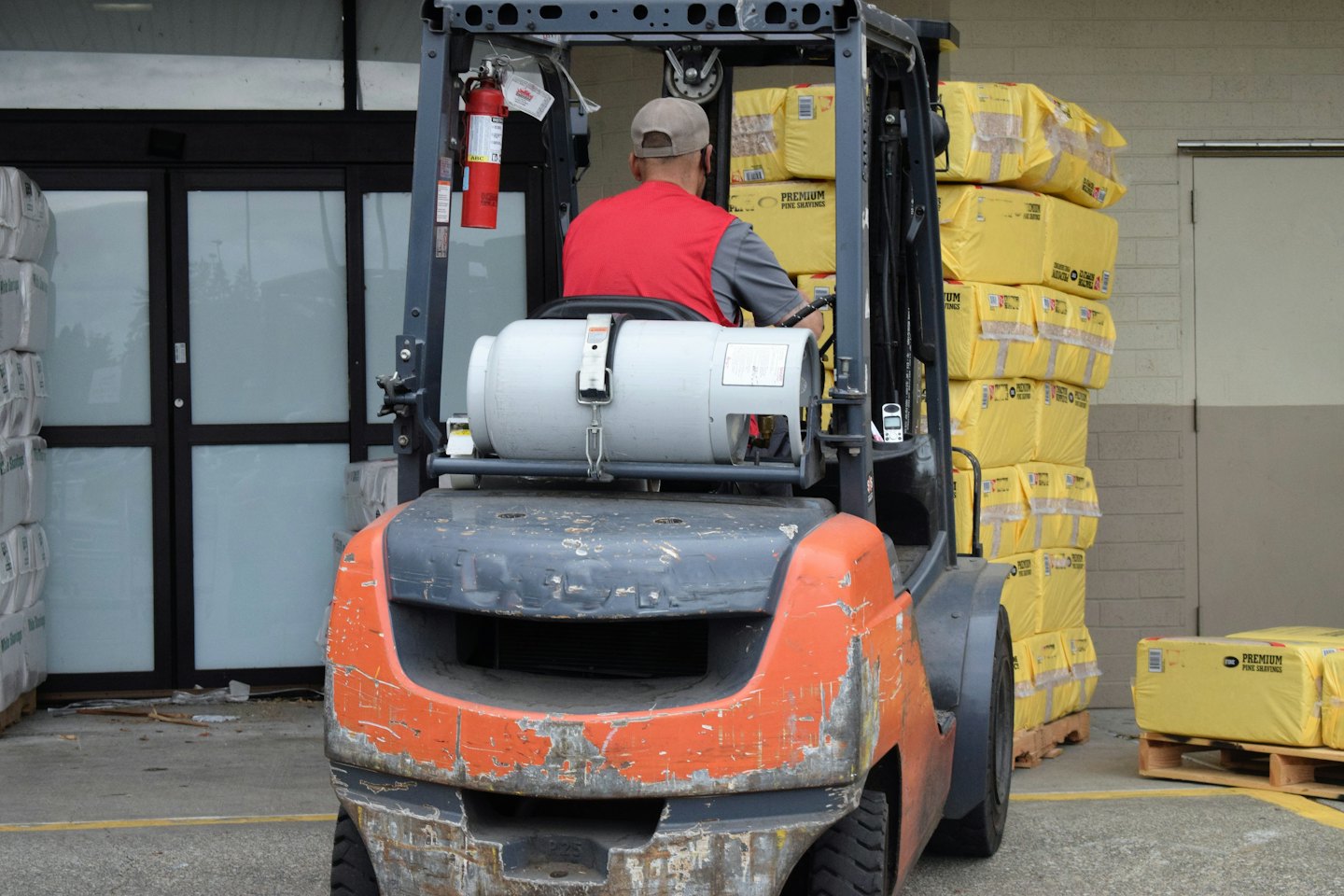 Trabajador conduce montacargas naranja con inventario en muelle de carga.